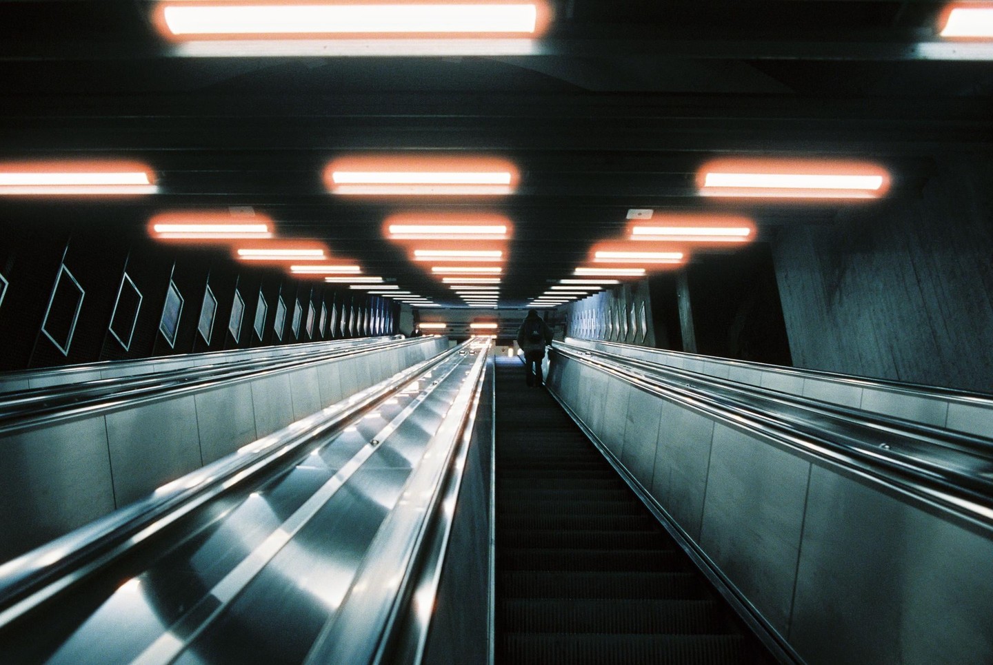 A person rides an escalator in a subway station illuminated by orange lights.