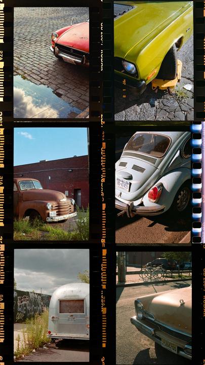 Six different photographs of vintage cars and a trailer are arranged in a grid, with film borders visible between them.