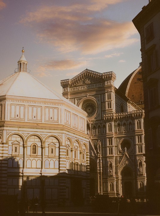 The Florence Cathedral and Baptistery are illuminated by the warm light of dusk.