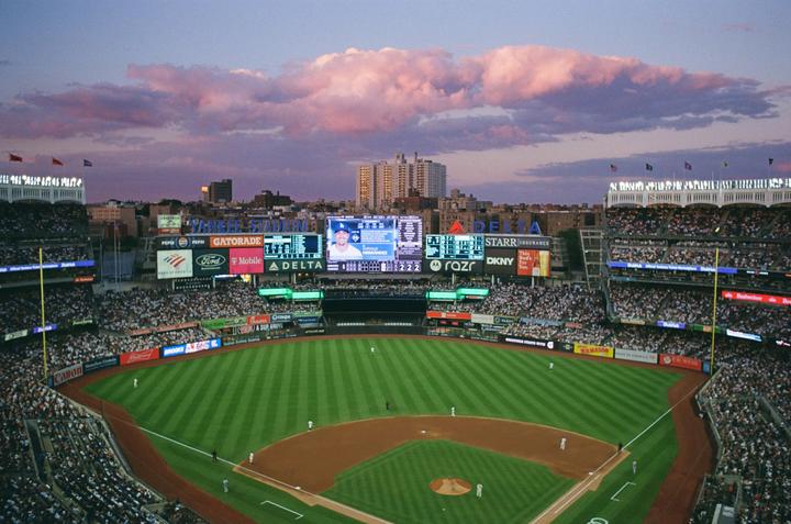A baseball game is underway in a stadium filled with spectators under a dramatic sky.