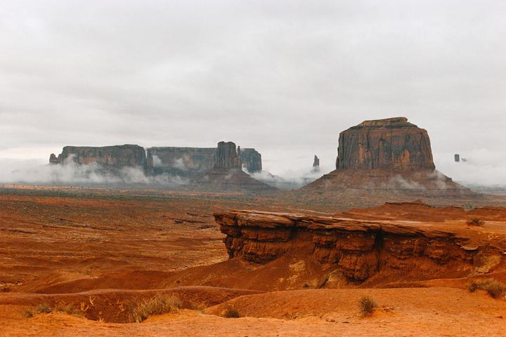 Fog rolls through a valley with large rock formations under a cloudy sky.