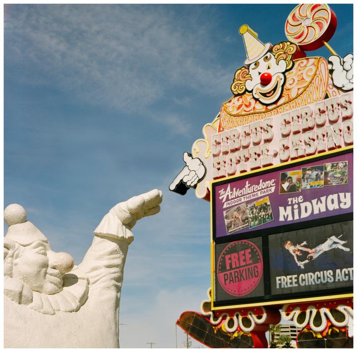 A large clown statue points towards a colorful sign for Circus Circus Casino and Adventuredome.