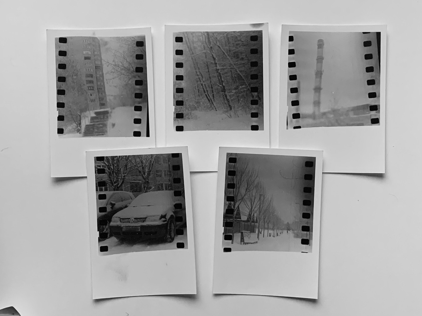 Five black and white prints with sprocket holes show snowy scenes including a building, a forest, a chimney, a car, and a street with trees.