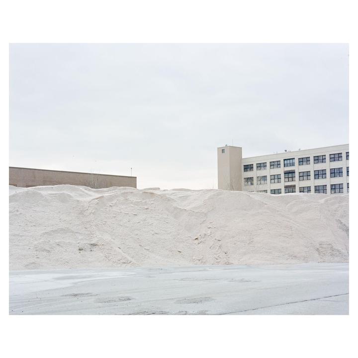 A large pile of white salt sits in front of two buildings under a cloudy sky.