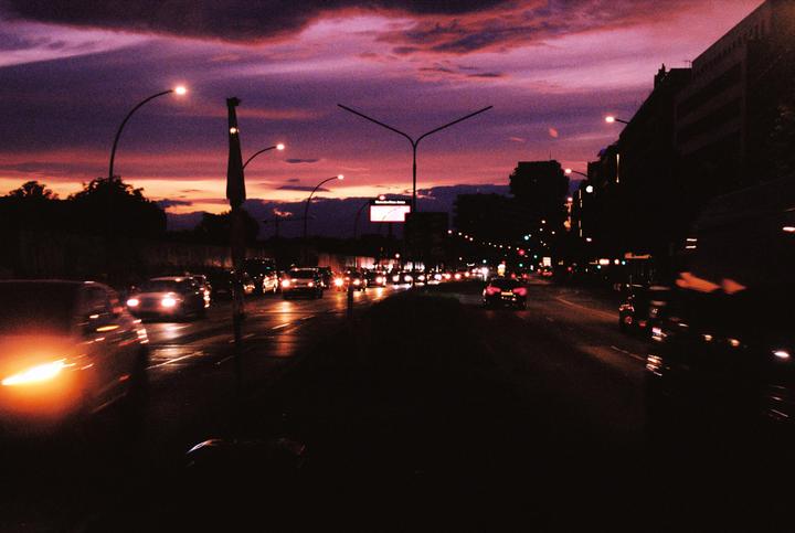 A street is filled with cars and streetlights under a dramatic purple and orange sunset.