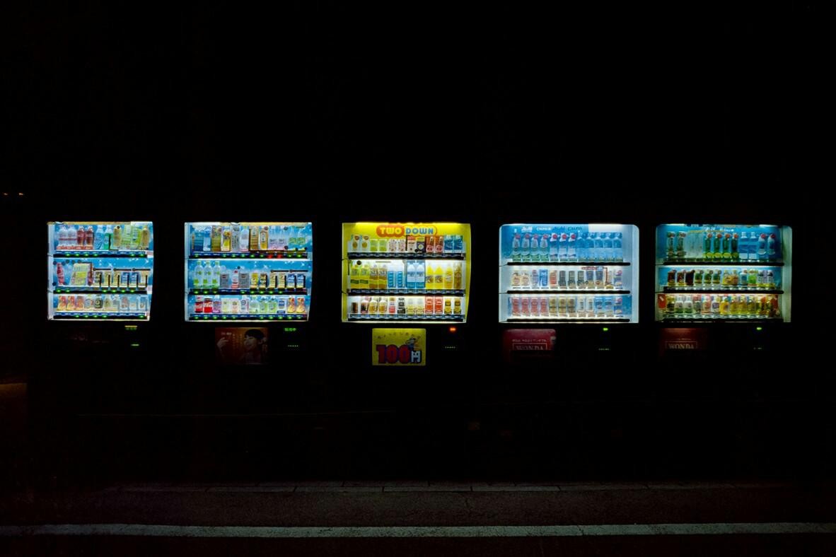 Five brightly lit vending machines stand in a row against a dark background at night.
