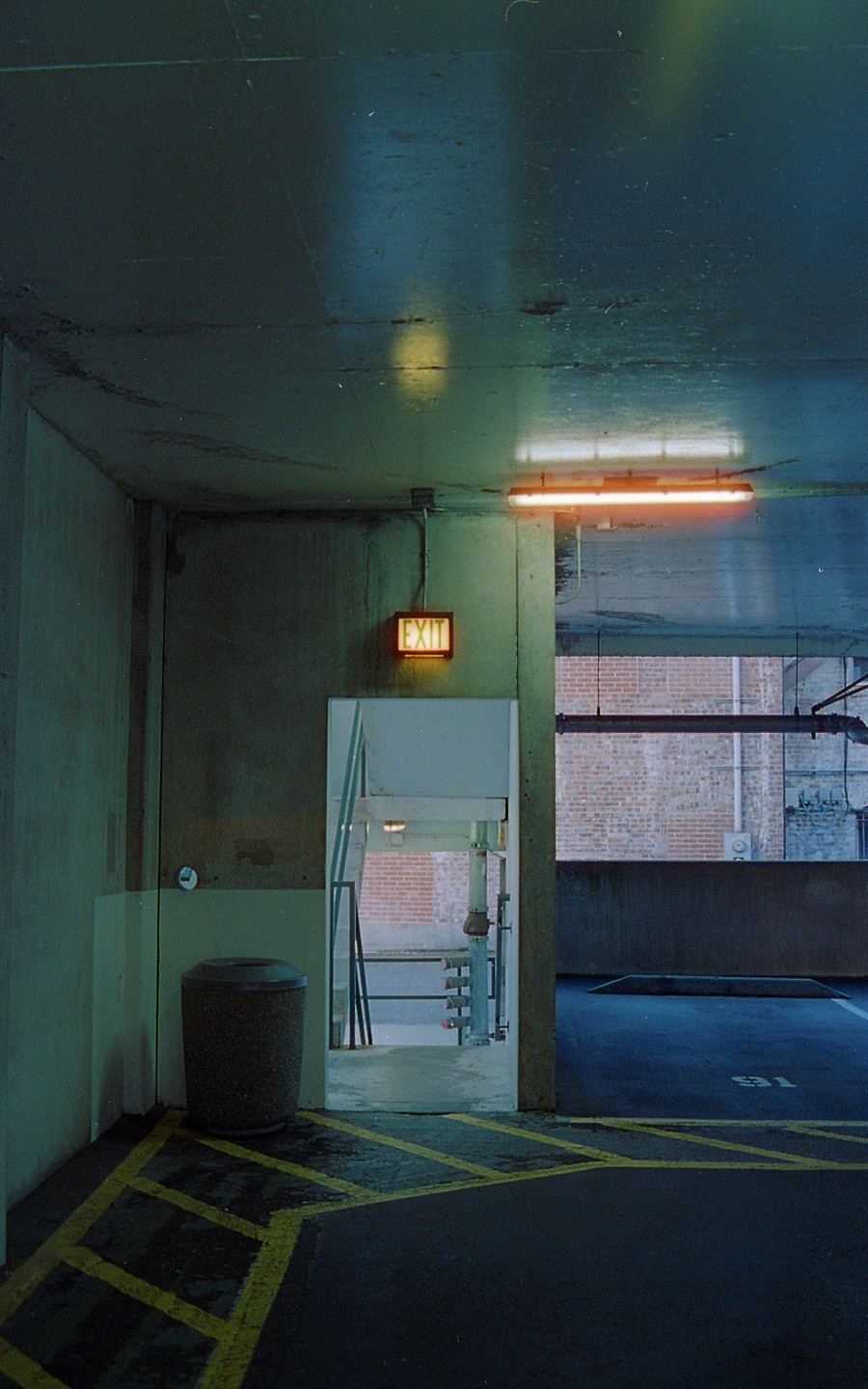 An exit sign hangs above a doorway in a parking garage with yellow striped pavement.