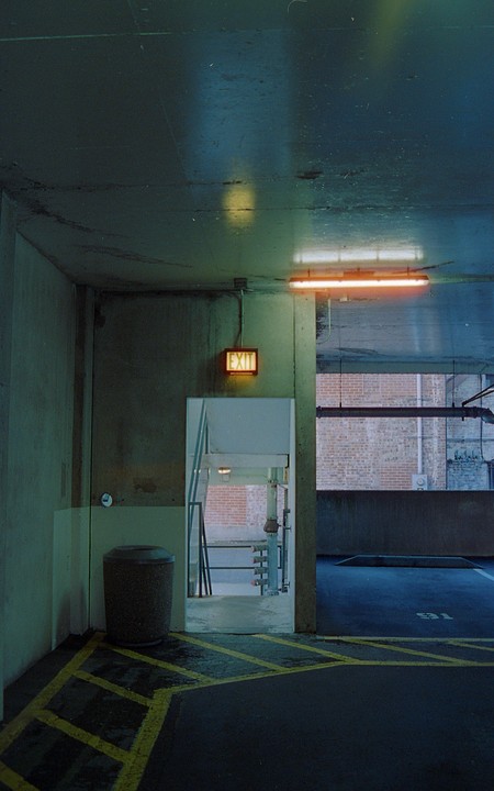 An exit sign hangs above a doorway in a parking garage with yellow striped pavement.