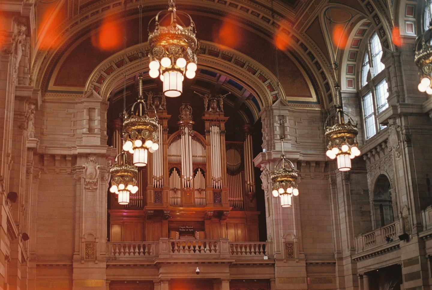 A large pipe organ is visible behind ornate chandeliers in a grand hall.