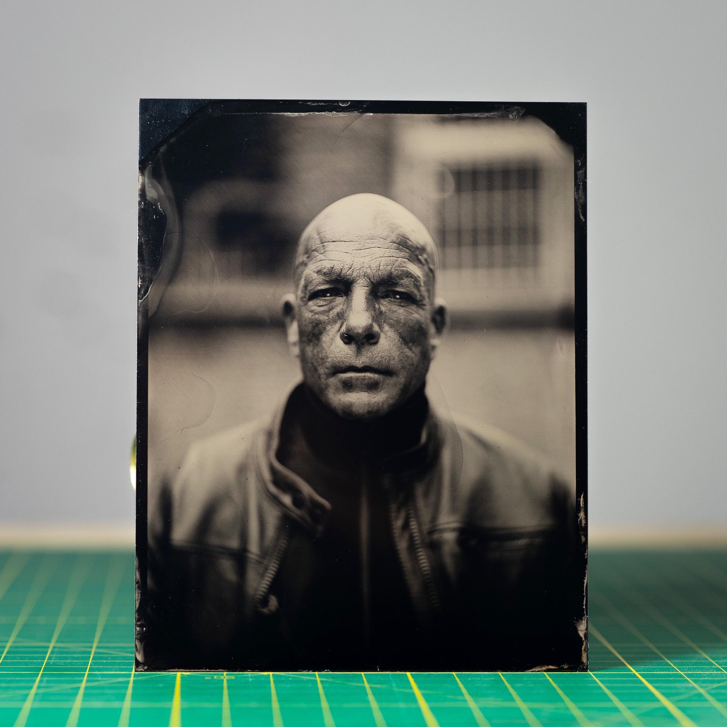 A bald man with a serious expression wears a jacket and turtleneck.