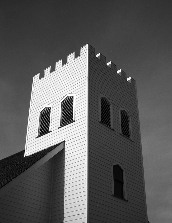 A tall, light-colored church tower with arched windows and a crenellated top stands against a dark sky.