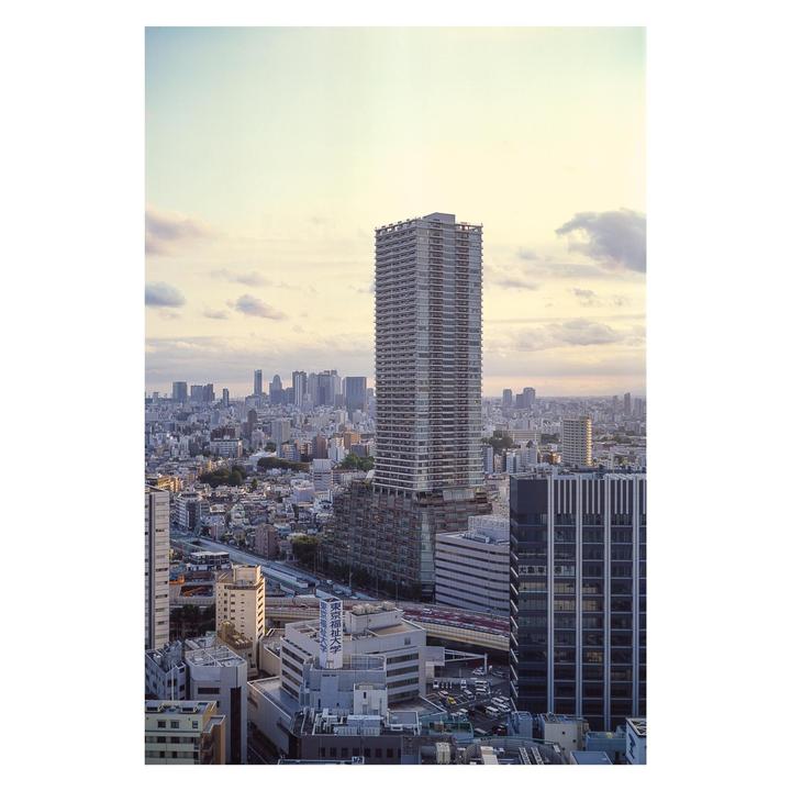 A tall skyscraper stands prominently in the middle of a sprawling city with many buildings under a cloudy sky.