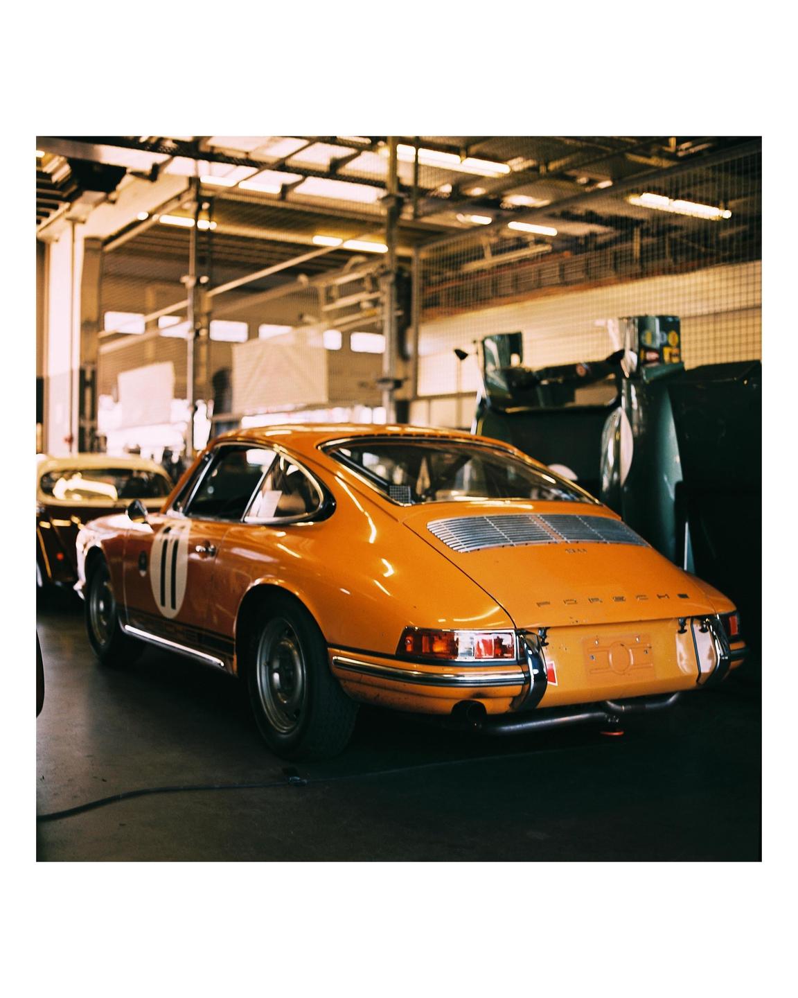 An orange vintage sports car with the number 11 on its side is parked in a garage.