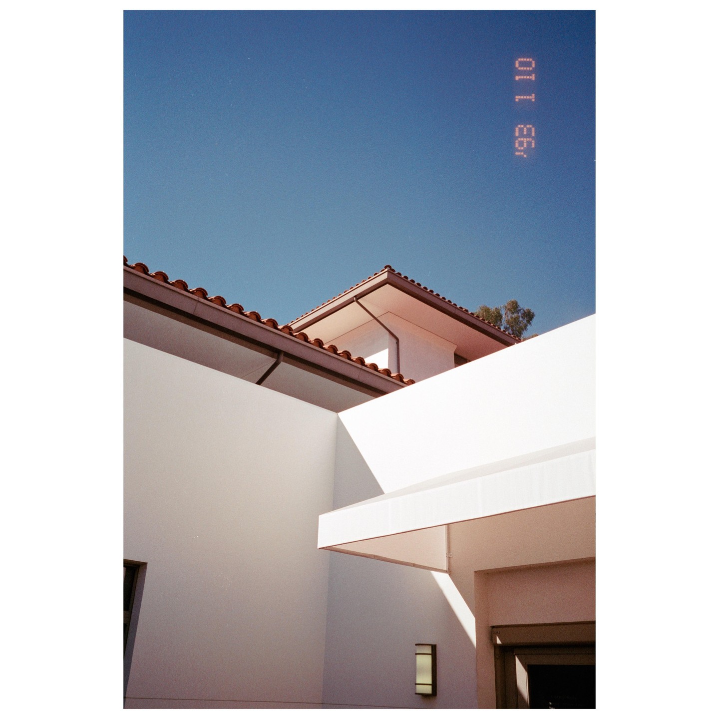 A building with white walls and a red tile roof is shown against a clear blue sky.