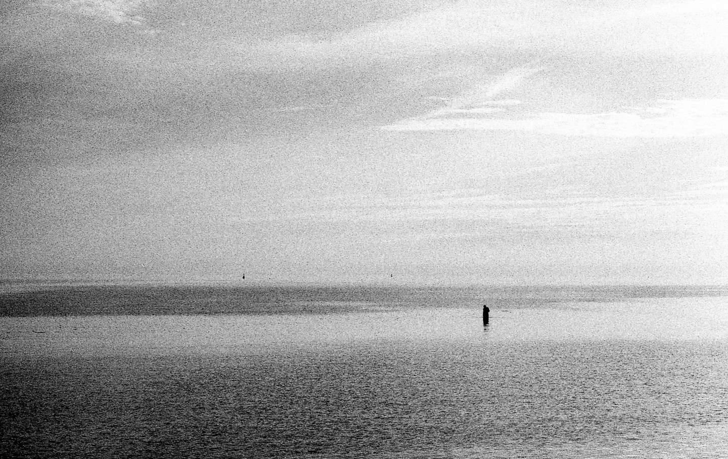 A lone figure stands in the water under a cloudy sky.