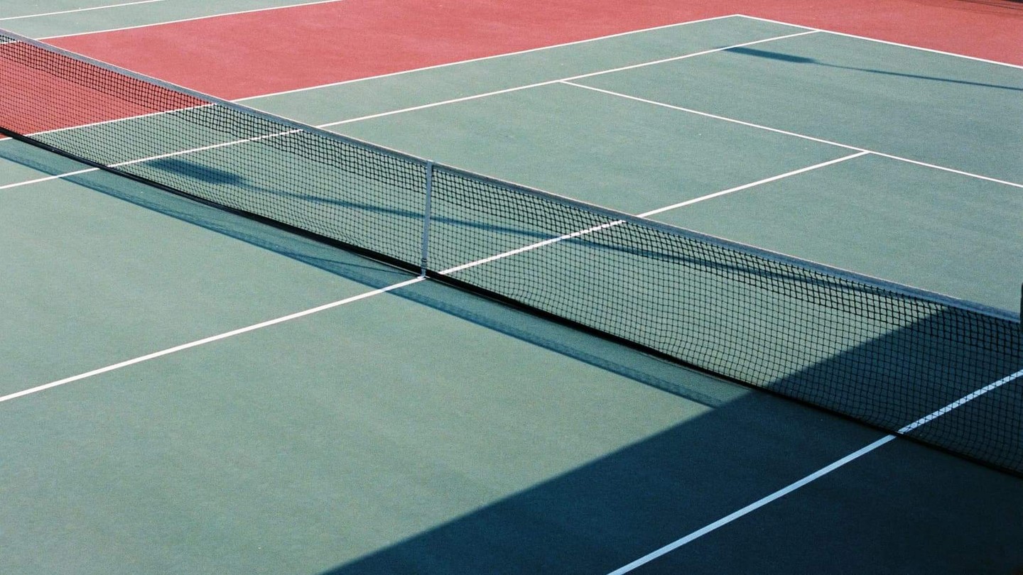 A tennis court with a net casts a shadow across the green surface.