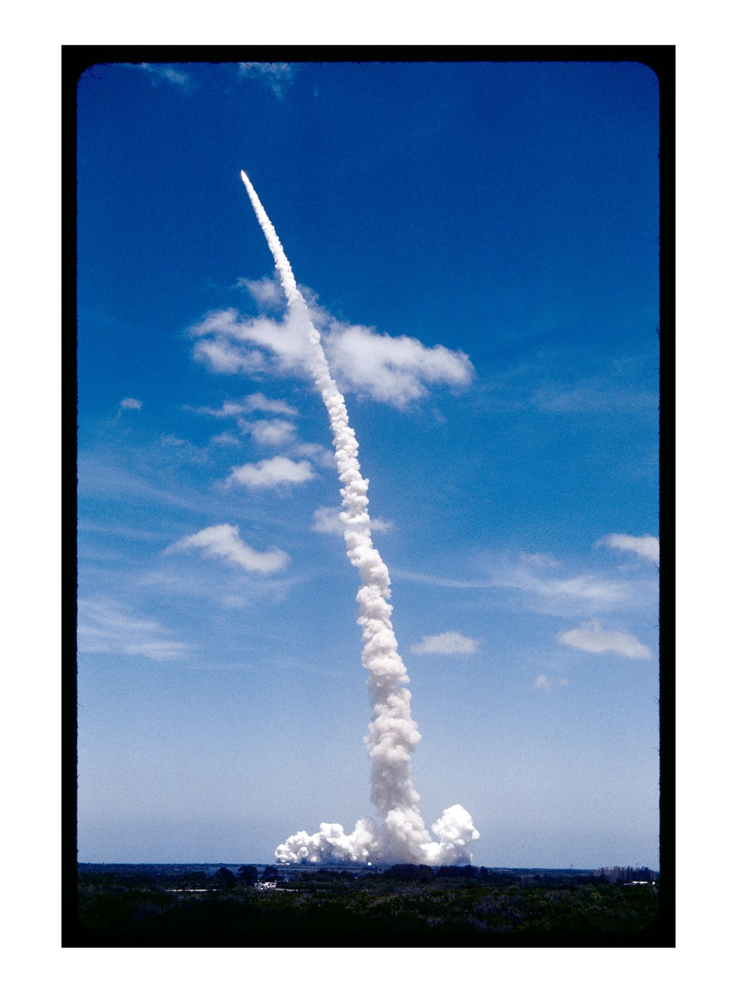 A rocket launches into a clear blue sky, leaving a long trail of white smoke.