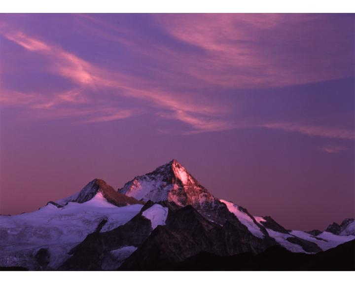 Snow-capped mountains are visible under a vibrant purple and pink sky.