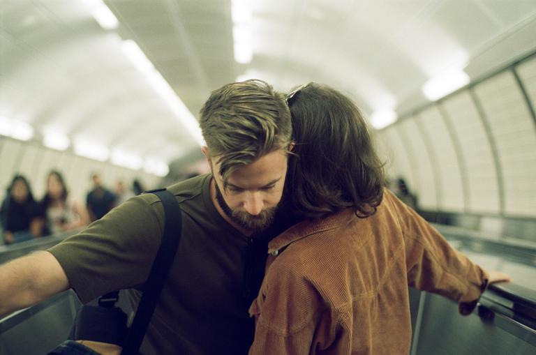 A man and a woman stand close together on an escalator in a subway tunnel.