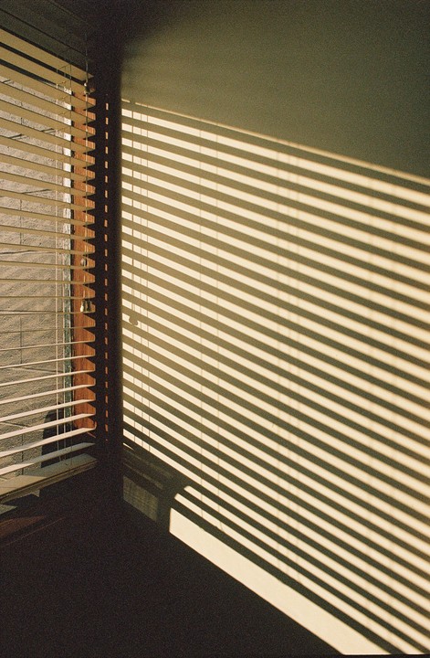 Sunlight streams through horizontal blinds, casting striped shadows across a wall and floor.