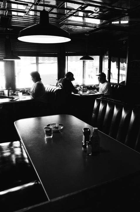 Three people sit in booths at a diner with an empty table in the foreground.