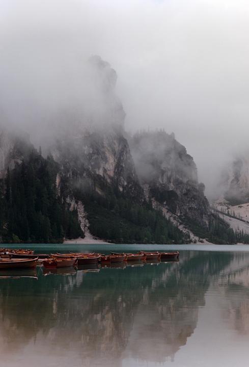 Wooden rowboats float on a lake surrounded by mountains shrouded in fog.