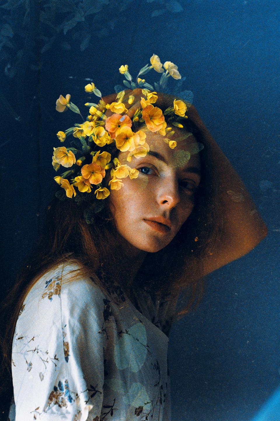 A woman with long hair and a floral dress has yellow flowers superimposed over her head and face.