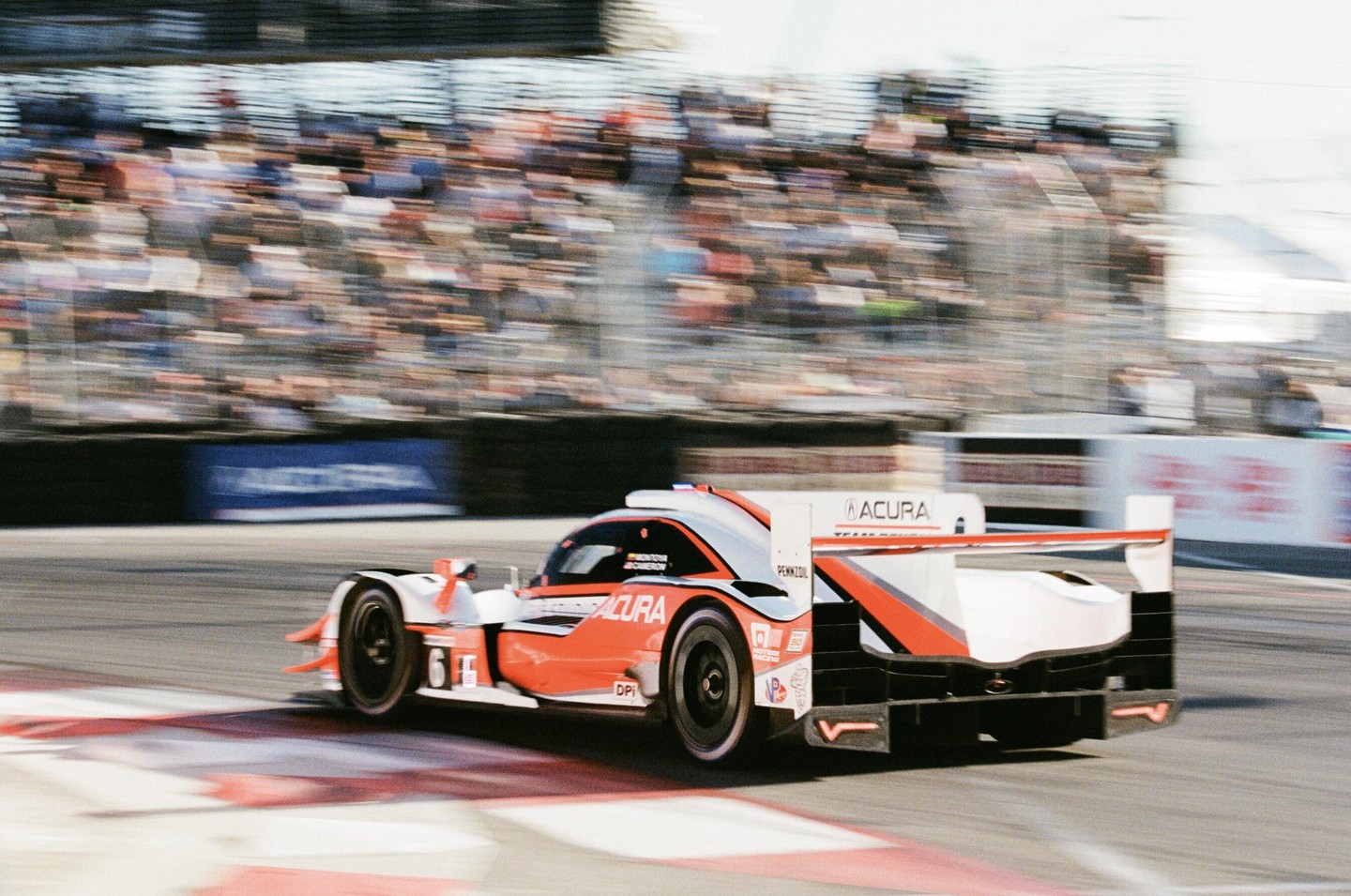 A red and white race car speeds around a track with blurred spectators in the background.