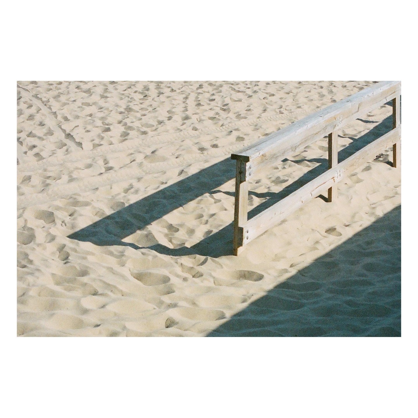 A wooden fence casts a long shadow across a sandy beach.