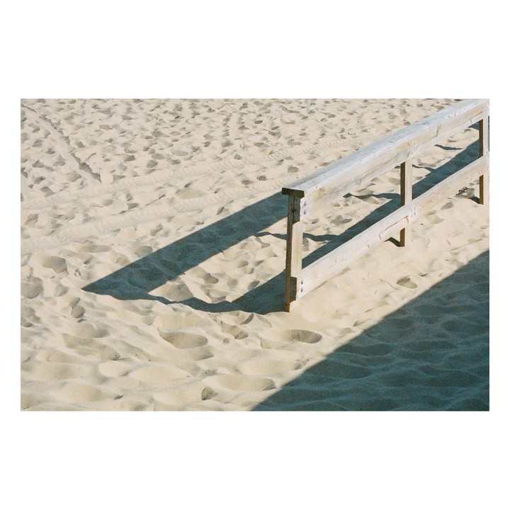 A wooden fence casts a long shadow across a sandy beach.