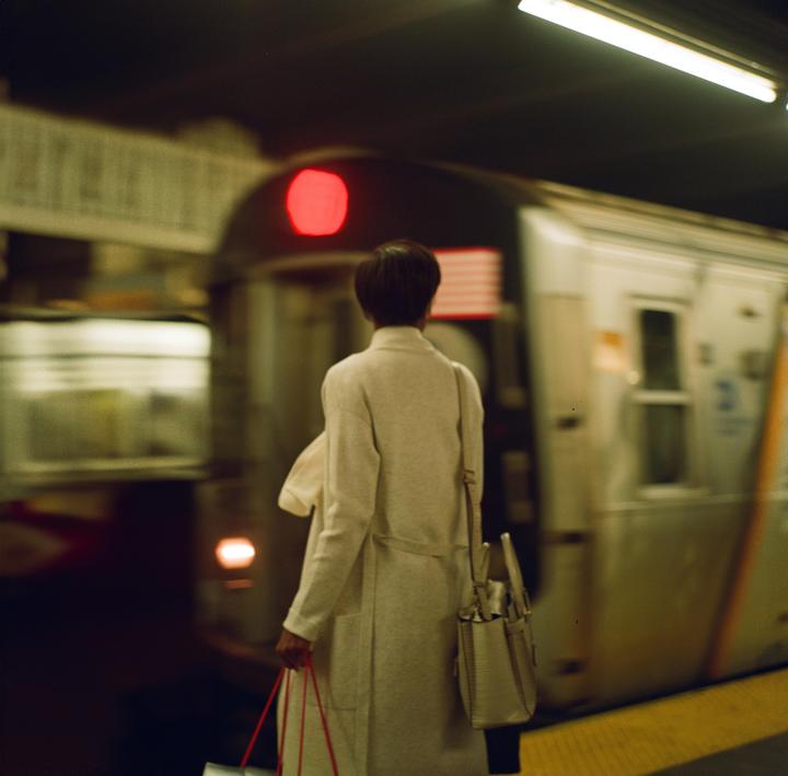 A woman stands on a subway platform as a train pulls into the station.