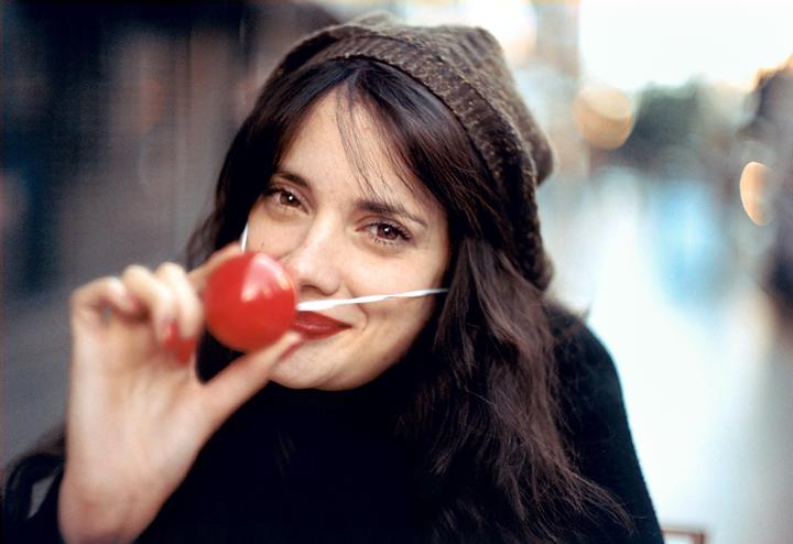 A woman wearing a knit hat and a red clown nose smiles at the camera.