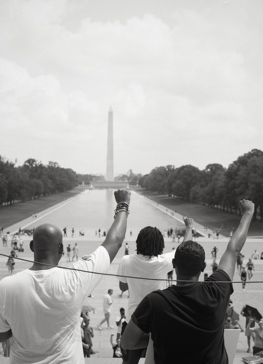 Three men with raised fists look towards the Washington Monument across the Reflecting Pool.