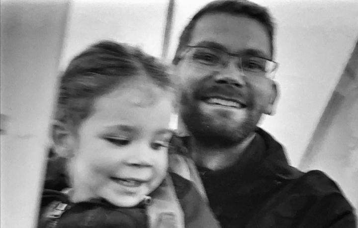 A man with glasses and a beard smiles next to a young child with a similar smile.