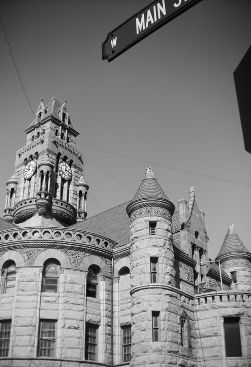 A black and white low-angle shot shows a stone building with a clock tower and turrets, with a street sign for Main Street in the upper right.