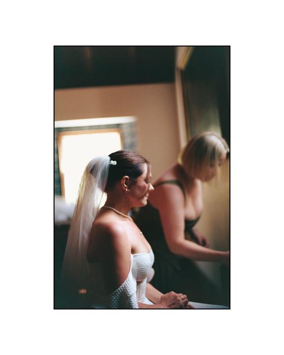 A woman in a wedding dress and veil sits next to another woman.