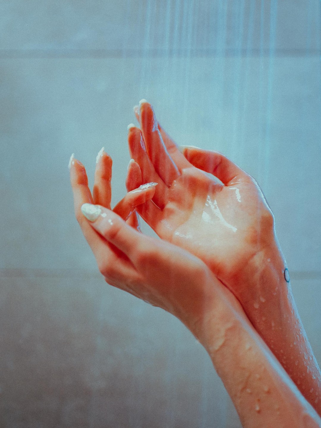 Two hands are held under running water, catching droplets.