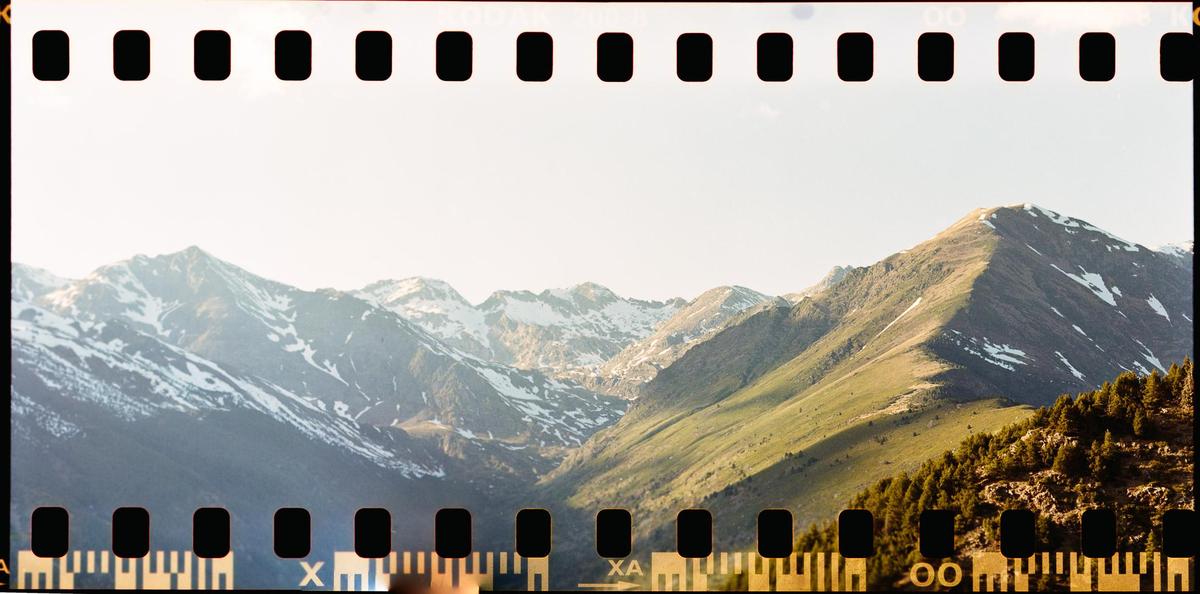 A mountain range with patches of snow and green slopes is visible under a bright sky.