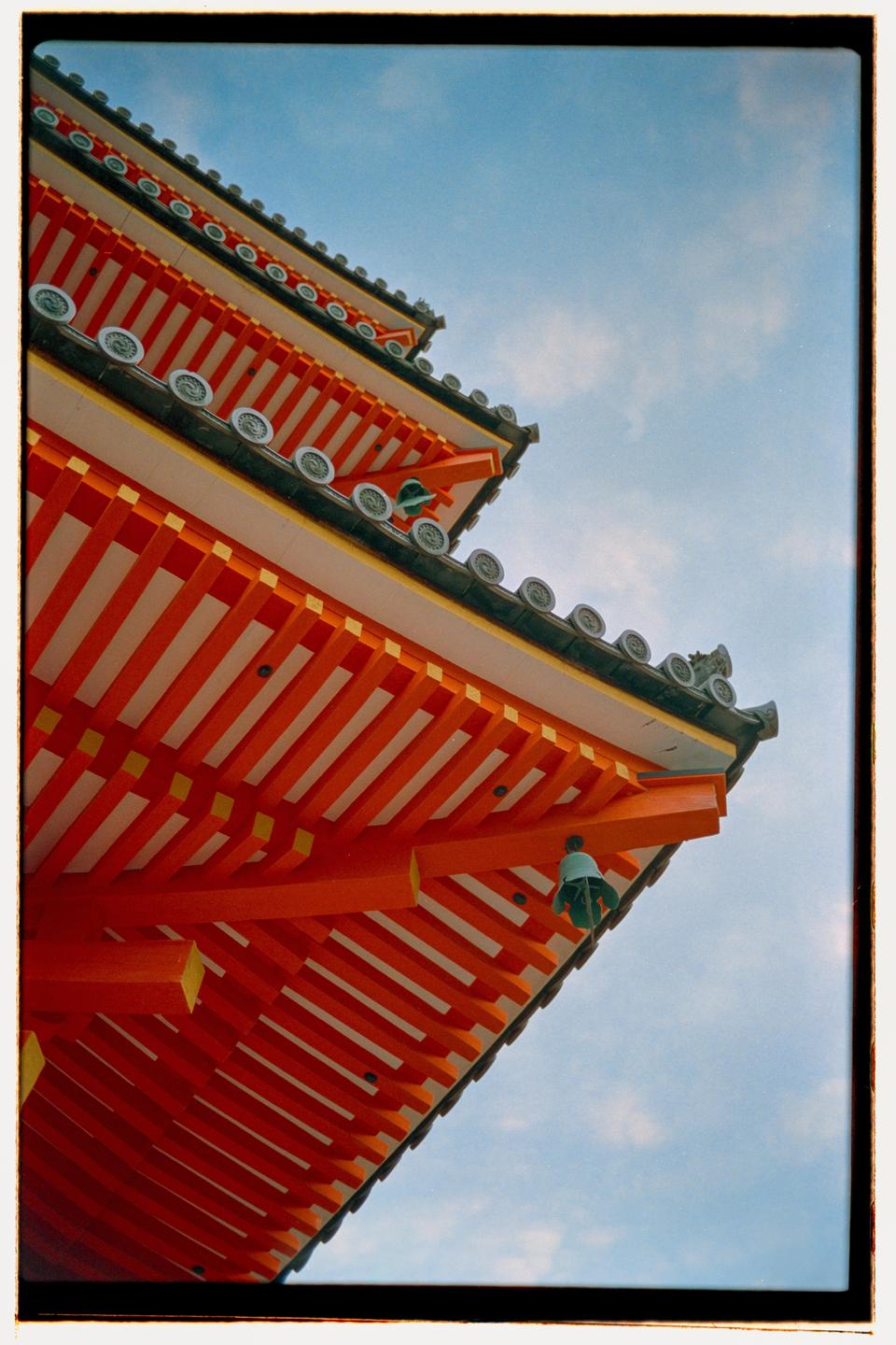 A low-angle view shows the tiered orange and white eaves of a temple against a blue sky.