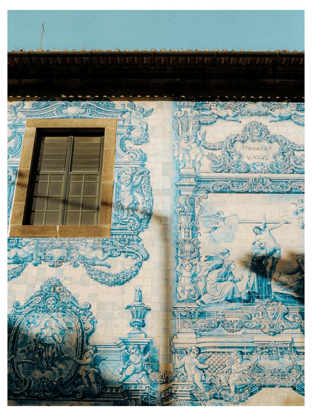 A building facade is covered in blue and white azulejo tiles depicting religious scenes and figures, with a single window on the left.