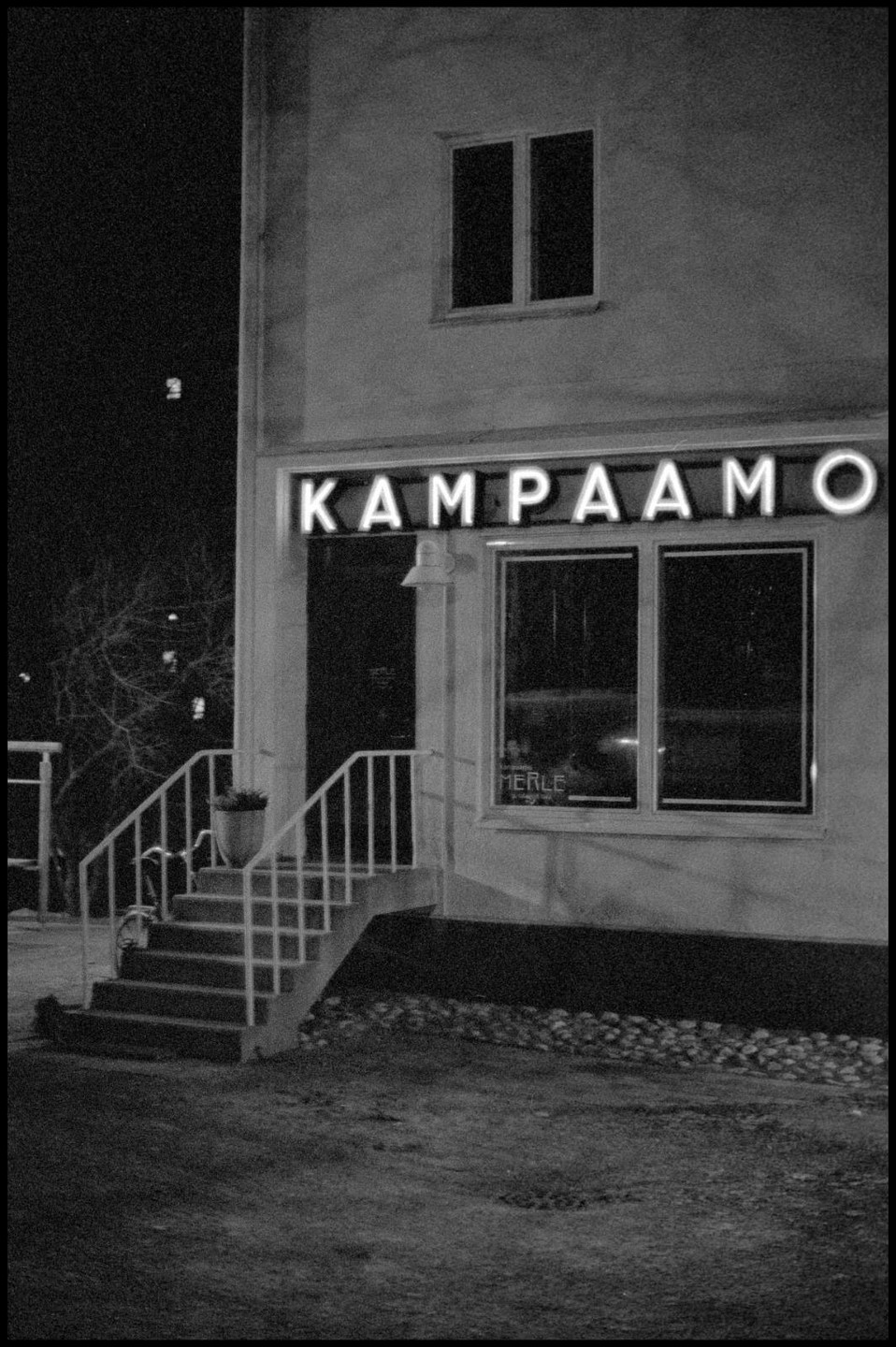 A building with a neon sign that reads "Kampaamo" is visible at night.