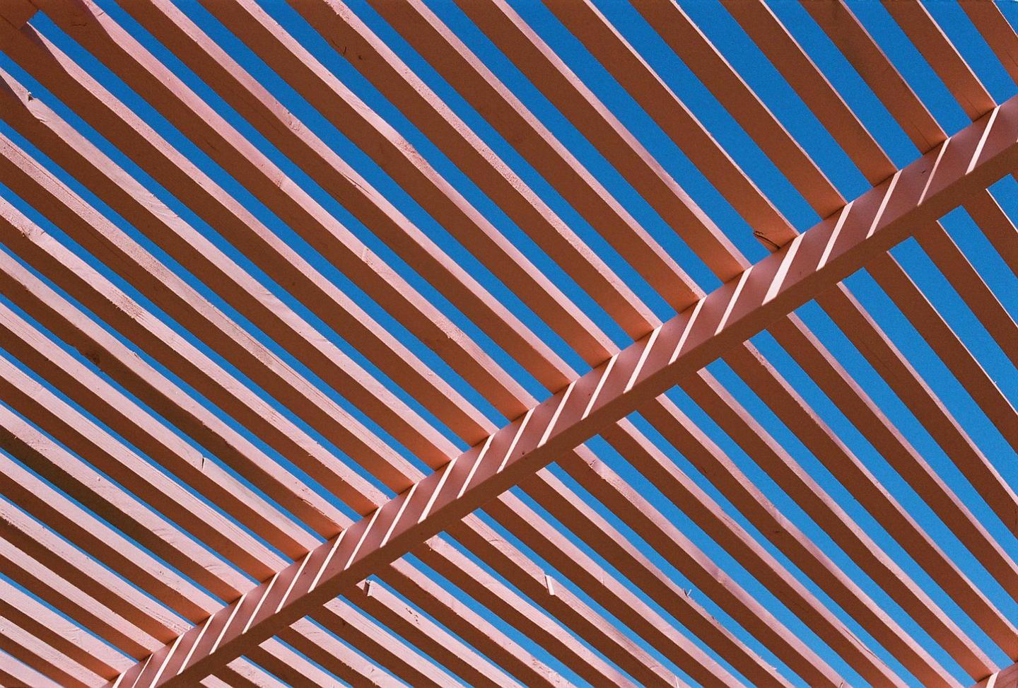 A wooden pergola casts shadows against a bright blue sky.