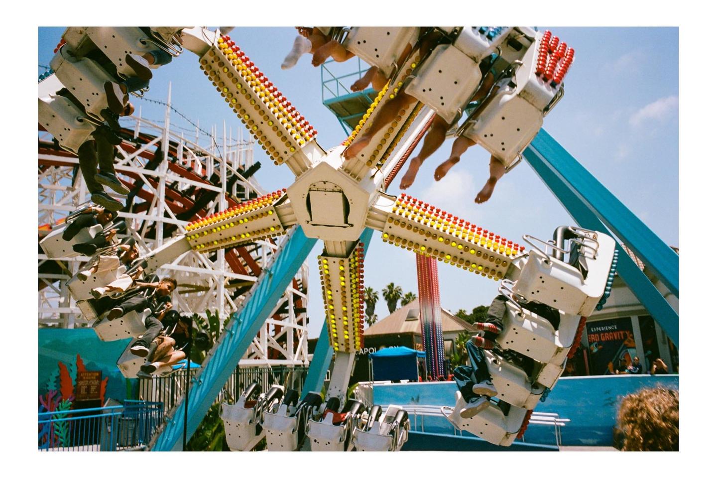 People are riding a spinning amusement park ride with a roller coaster in the background.