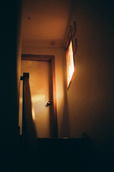 Sunlight streams through a window onto a door and a banister in a dimly lit room.