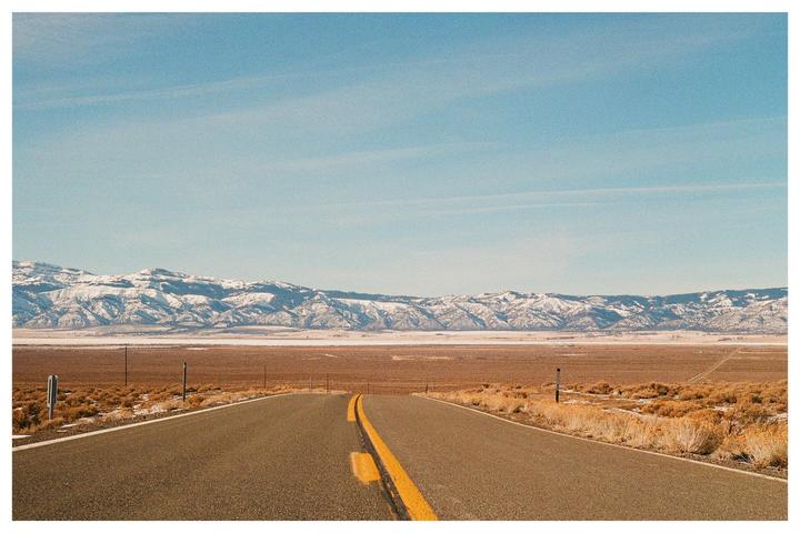 A long road stretches towards snow-capped mountains under a clear sky.