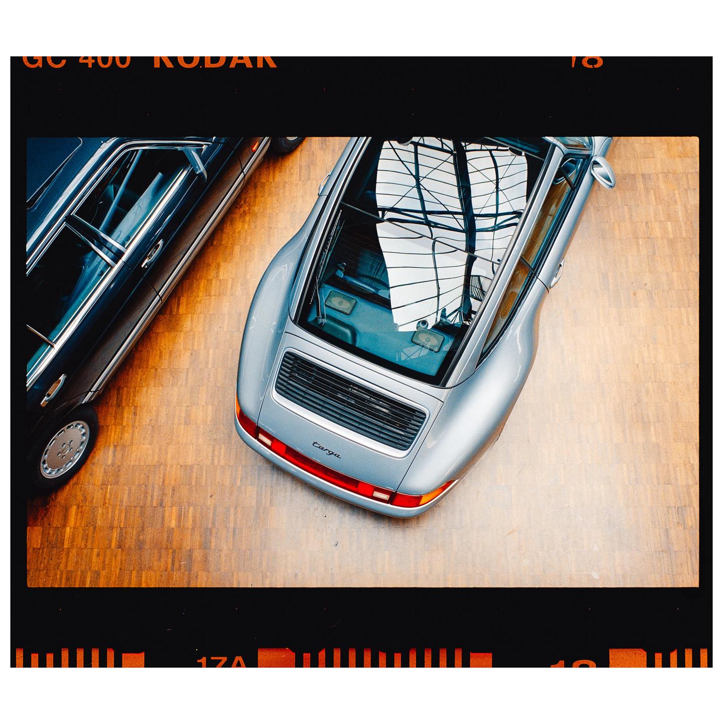 Two classic cars are parked on a wooden floor, viewed from above.