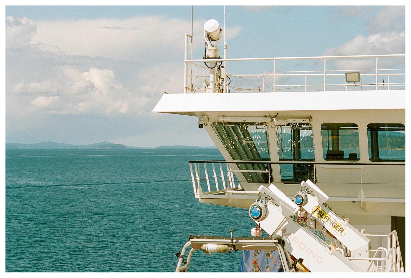 A white boat with a crane is on the water with mountains in the distance under a cloudy sky.