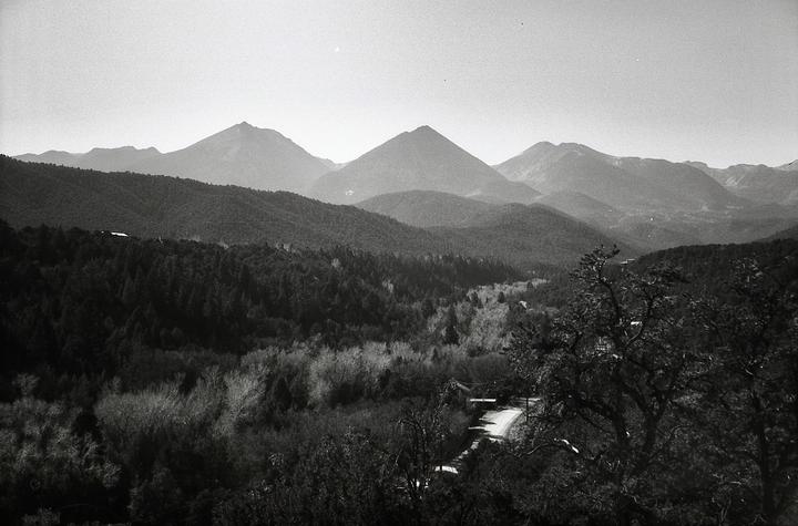 A winding road leads through a valley of trees towards distant mountains under a hazy sky.