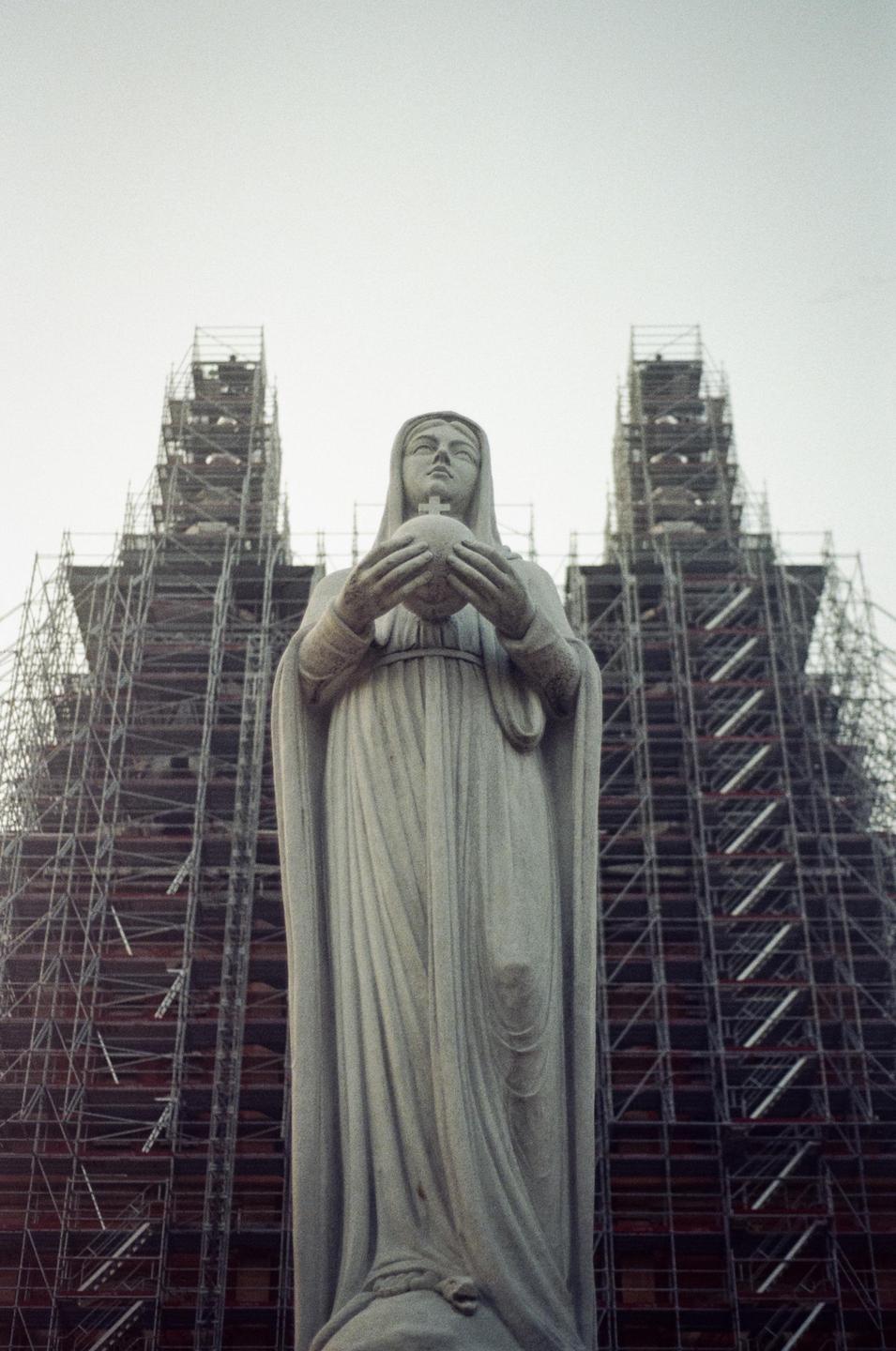A statue of a woman holding a globe stands in front of a building covered in scaffolding.
