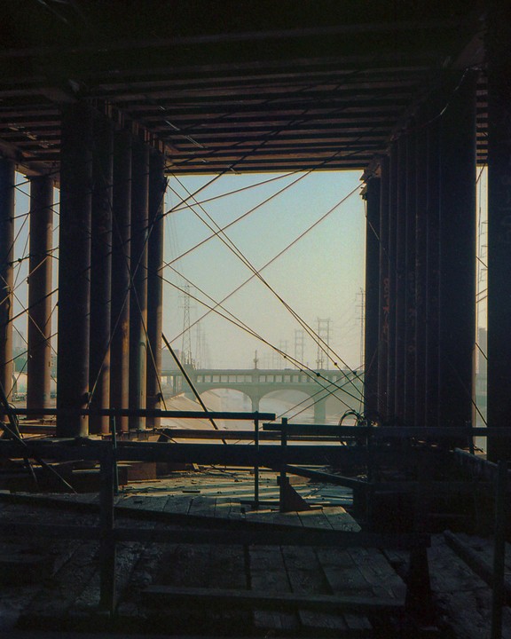 A bridge is visible through a gap in a structure with many pillars and wires.